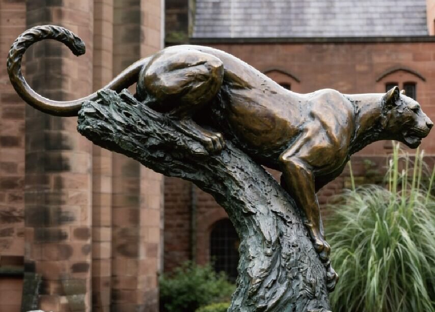 custom bronze leopard statue on a tree trunk in an outdoor garden