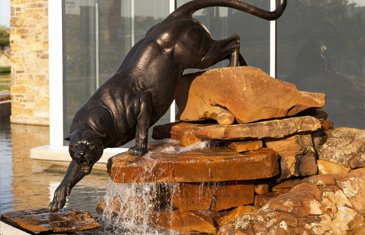 Custom life-size bronze panther wildlife sculpture jumping over a rock water feature in a high-end private estate garden