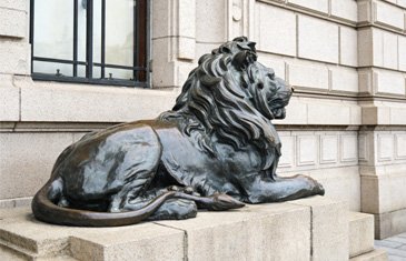 Majestic seated bronze lion statue in front of a commercial building entrance serving as a symbol of strength and luxury brand identity