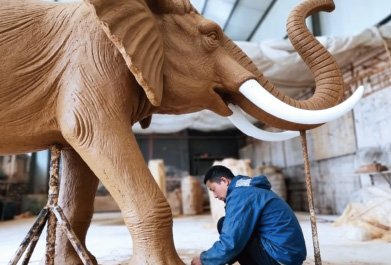 Master sculptor working on the realistic facial features and tusks of a massive elephant clay sculpture
