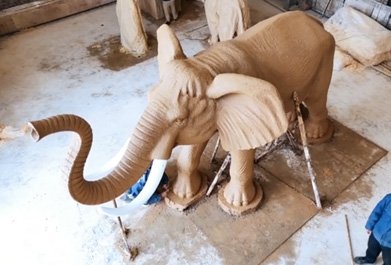 Top-down perspective of a monumental elephant clay model showing the scale and dynamic trunk pose