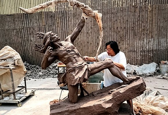A master artist hand-sculpting a dynamic figure, illustrating our Design Conceptualization & Detailed Coordination process and the creation of a 1:1scale clay maquette for client approval.