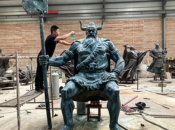Artisan applying a protective layer to a monumental bronze warrior statue, illustrating Wensculp's Protection Process for Custom Sculptures After Painting and Automotive-Grade Clear Coat Encapsulation for long-term Environmental Resilience .