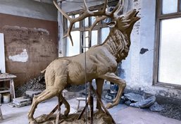 A master artist hand-sculpting a 1:1 scale clay model of a large elk, demonstrating the highest level of artistic fidelity in the foundry process.
