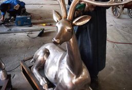 Master artisan applying advanced chemical patina finish to a bronze deer sculpture for exceptional weather resistance and aesthetic depth.