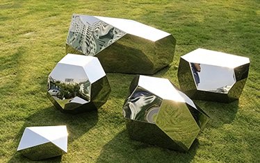 Geometric mirror-polished stainless steel sculpture on a lawn