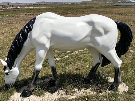 white grazing fiberglass horse statue with head lowered
