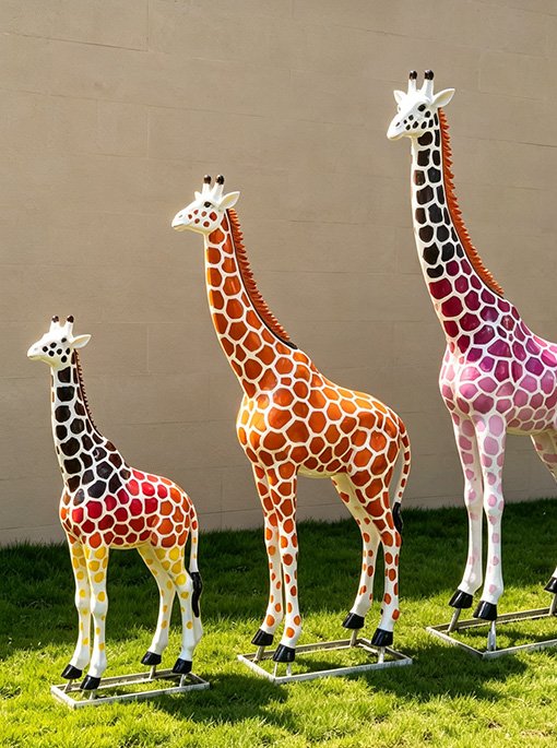 three custom fiberglass giraffe statues at different heights on grass