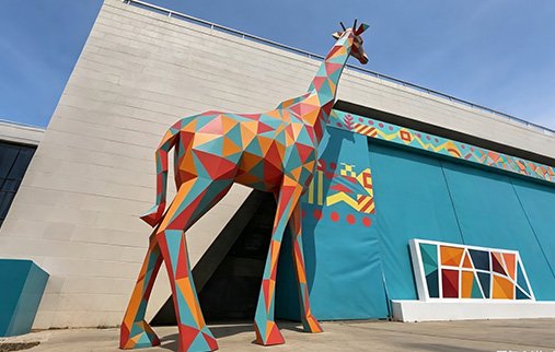giant colorful geometric fiberglass giraffe statue outside a building