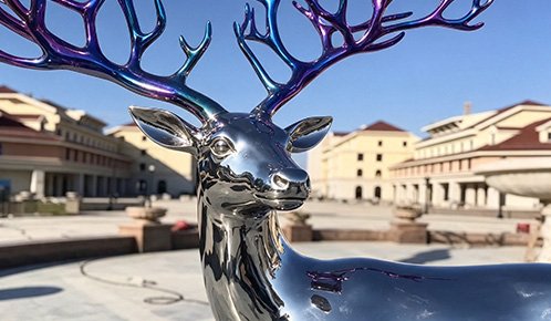 Life-size realistic stainless steel deer sculpture in a plaza