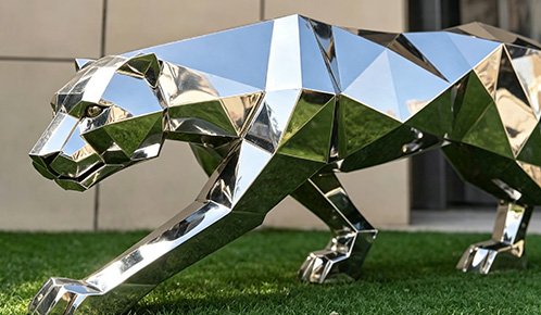 Geometric faceted stainless steel panther sculpture on a lawn