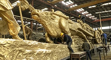 Craftsmen applying surface finishing to a large bronze sculpture in the workshop
