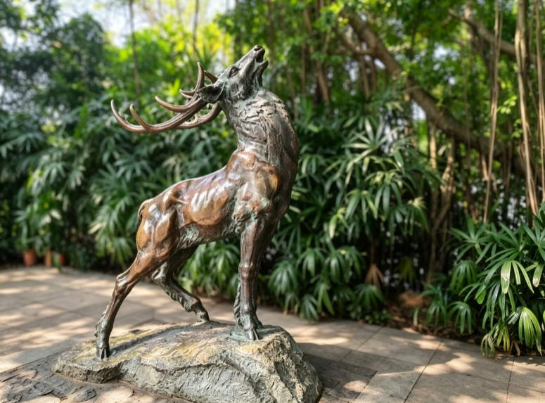 Deer Call bronze stag animal sculpture on a natural rock base among green foliage in Guangzhou's Luhu Park, roughly 1.8 m tall in a rearing, bugling pose
