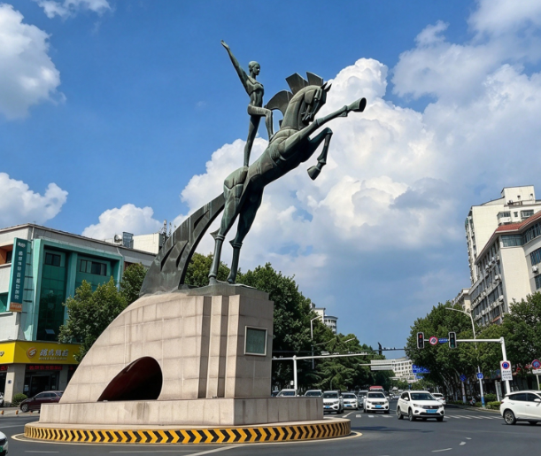 Large bronze horse sculpture over 10 m tall of a knight on a rearing horse, set on a stone base at a city-center plaza roundabout with cars passing by
